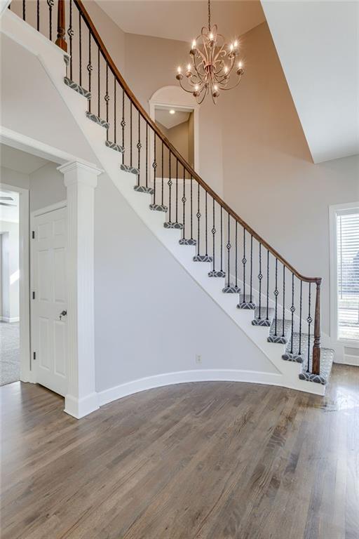 stairway featuring a notable chandelier, baseboards, a high ceiling, and wood finished floors