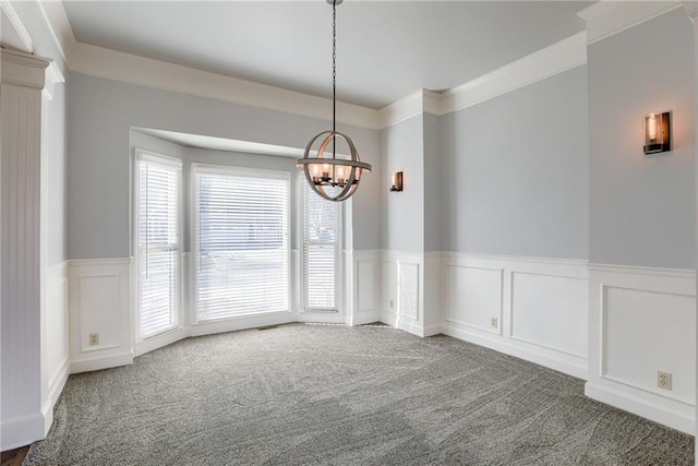 unfurnished room with a wainscoted wall, ornamental molding, carpet flooring, a chandelier, and ornate columns