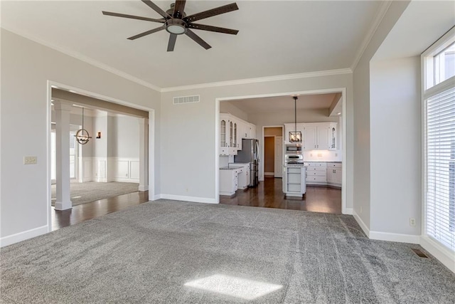 unfurnished living room with crown molding, a ceiling fan, visible vents, and dark colored carpet