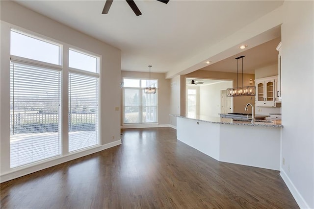 kitchen with light stone countertops, dark wood-type flooring, glass insert cabinets, white cabinetry, and ceiling fan with notable chandelier