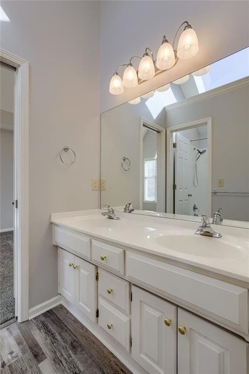 full bath with double vanity, wood finished floors, baseboards, and a sink