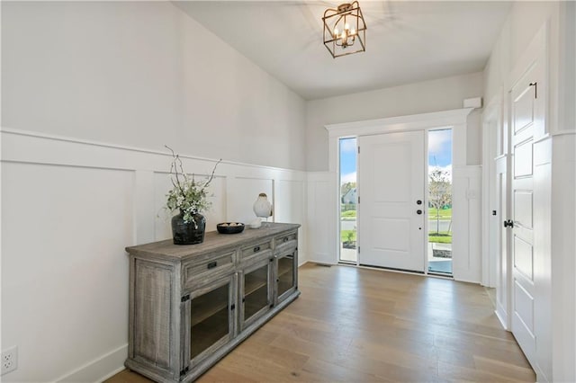 foyer entrance featuring a chandelier, wainscoting, a decorative wall, and light wood finished floors