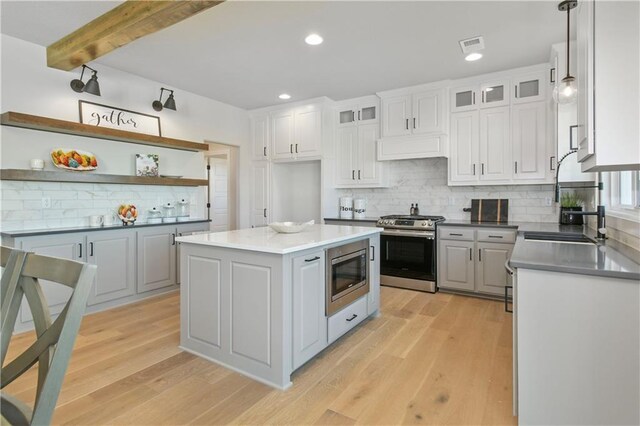 kitchen featuring open shelves, appliances with stainless steel finishes, light wood-type flooring, and a kitchen island