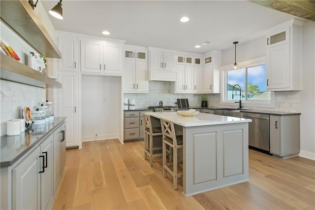 kitchen with a center island, light wood finished floors, stainless steel dishwasher, white cabinets, and a sink