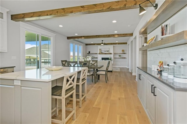 kitchen featuring light wood-type flooring, white cabinets, beamed ceiling, and decorative backsplash