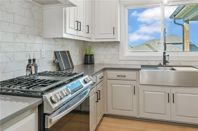 kitchen featuring tasteful backsplash, light wood-style flooring, white cabinets, a sink, and stainless steel gas range oven