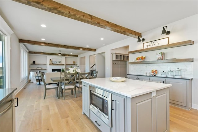 kitchen featuring a kitchen island, beamed ceiling, stainless steel appliances, gray cabinetry, and a fireplace