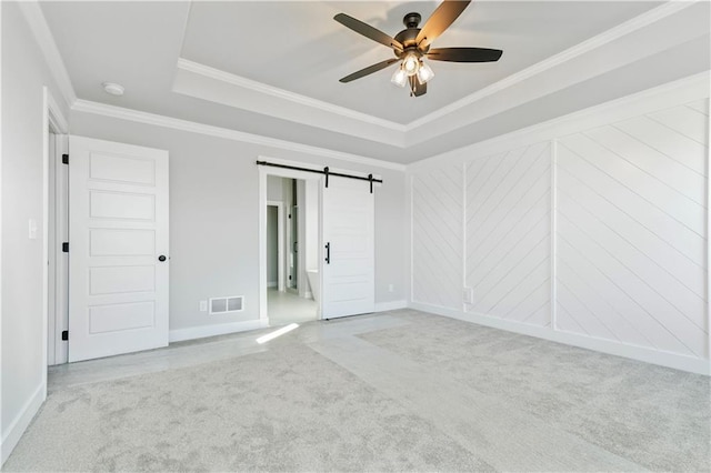 spare room featuring carpet floors, a tray ceiling, visible vents, a barn door, and ornamental molding