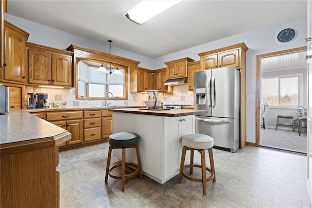 kitchen featuring decorative backsplash, stainless steel refrigerator with ice dispenser, under cabinet range hood, a kitchen bar, and a center island