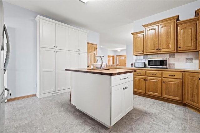 kitchen featuring stainless steel microwave, a kitchen island, baseboards, decorative backsplash, and white cabinets