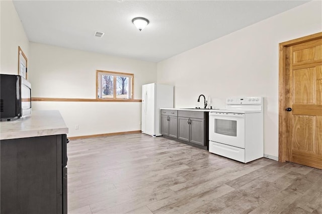 kitchen with white appliances, light wood-style flooring, light countertops, and a sink