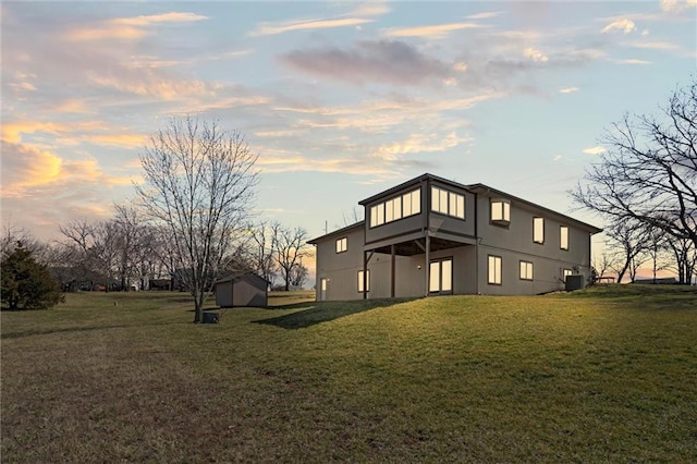 back of house featuring a storage unit, central air condition unit, stucco siding, a yard, and an outdoor structure