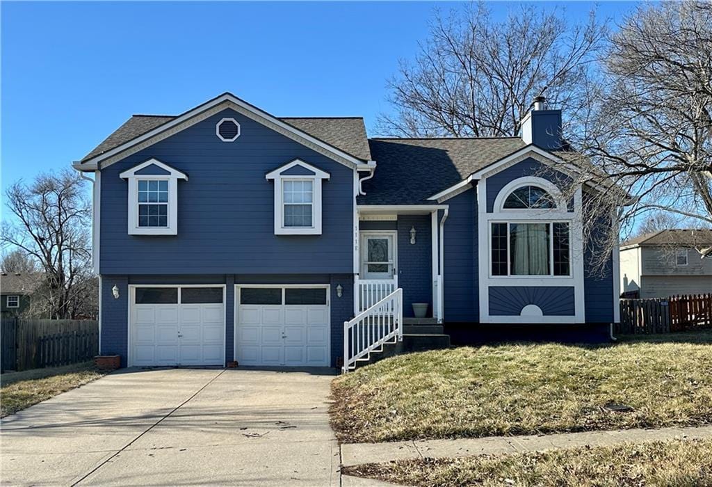 tri-level home featuring driveway, a chimney, an attached garage, and fence