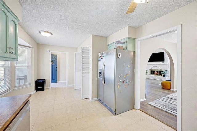 kitchen with a brick fireplace, a textured ceiling, appliances with stainless steel finishes, and green cabinetry