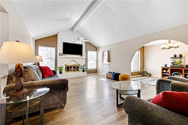 living area featuring a healthy amount of sunlight, a fireplace, lofted ceiling with beams, and hardwood / wood-style flooring