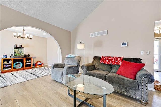 living area with arched walkways, a textured ceiling, a chandelier, wood finished floors, and visible vents