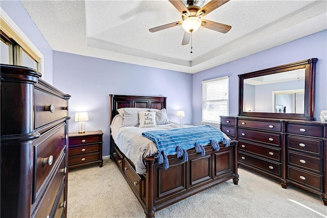 bedroom featuring a textured ceiling, ceiling fan, a raised ceiling, and light colored carpet