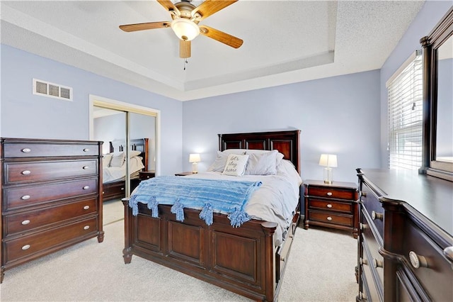 bedroom with light carpet, visible vents, a raised ceiling, and a closet