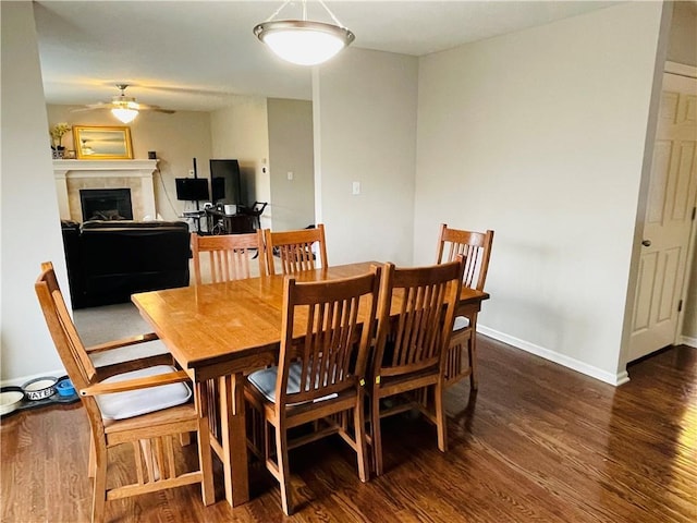 dining space with baseboards, wood finished floors, a ceiling fan, and a tile fireplace