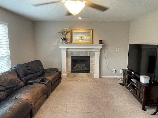 carpeted living area with a tiled fireplace, a textured ceiling, baseboards, and a ceiling fan