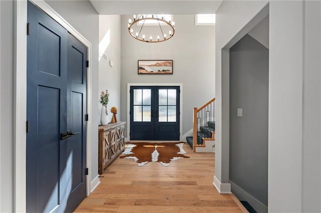 foyer featuring baseboards, light wood-type flooring, stairs, french doors, and a high ceiling