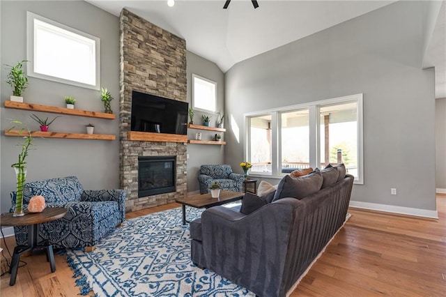 living area with baseboards, high vaulted ceiling, a stone fireplace, and wood finished floors