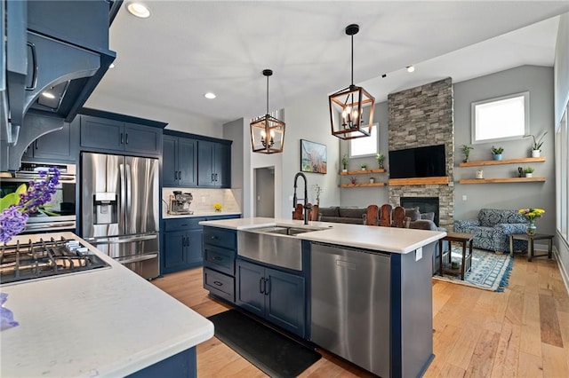 kitchen featuring a sink, blue cabinetry, stainless steel appliances, a stone fireplace, and light countertops