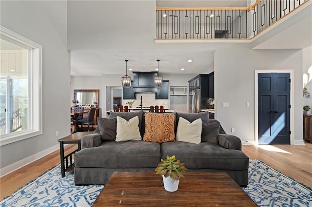 living area with recessed lighting, baseboards, light wood-type flooring, and a towering ceiling