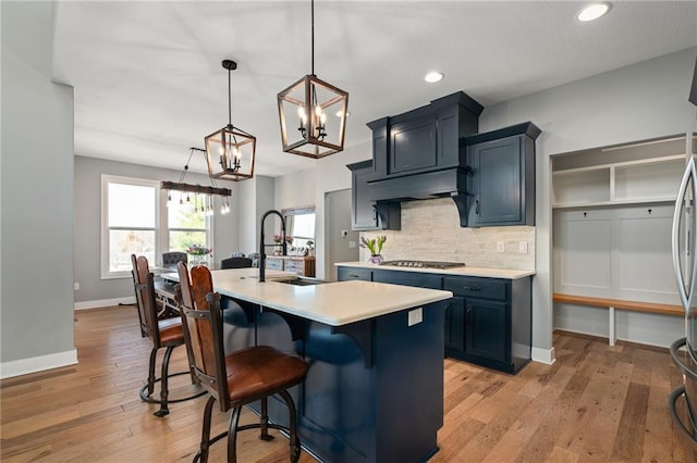 kitchen with a kitchen island with sink, a sink, tasteful backsplash, light wood-style floors, and light countertops