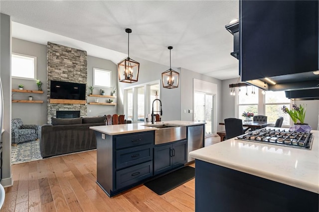 kitchen featuring light wood finished floors, a fireplace, a sink, light countertops, and appliances with stainless steel finishes