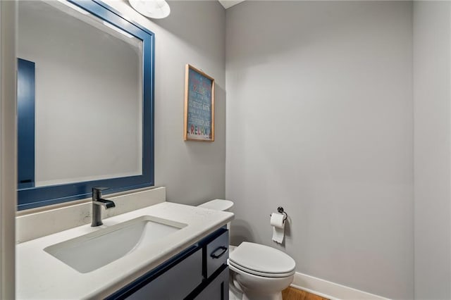 half bathroom featuring toilet, vanity, and baseboards