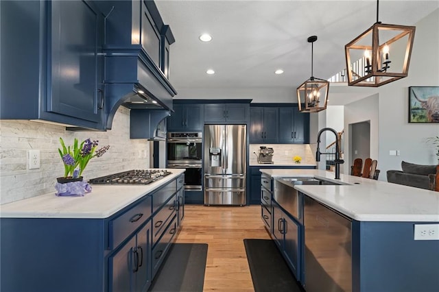 kitchen featuring light wood finished floors, blue cabinetry, a sink, stainless steel appliances, and light countertops