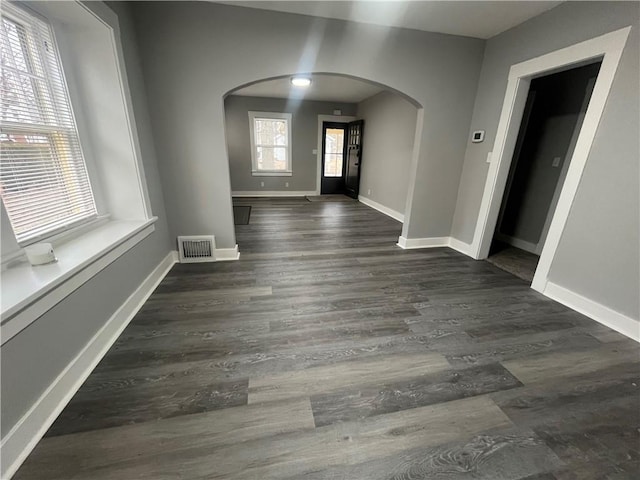 interior space featuring arched walkways, dark wood-style flooring, visible vents, and baseboards