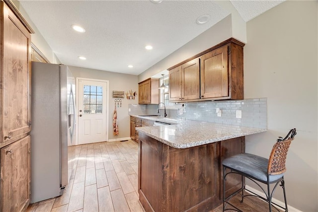 kitchen featuring wood finish floors, decorative backsplash, freestanding refrigerator, a sink, and a peninsula