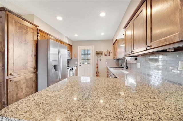 kitchen with stainless steel appliances, a sink, light stone counters, and tasteful backsplash