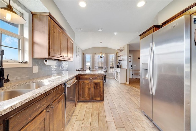 kitchen featuring lofted ceiling, stainless steel appliances, a peninsula, decorative backsplash, and light wood finished floors