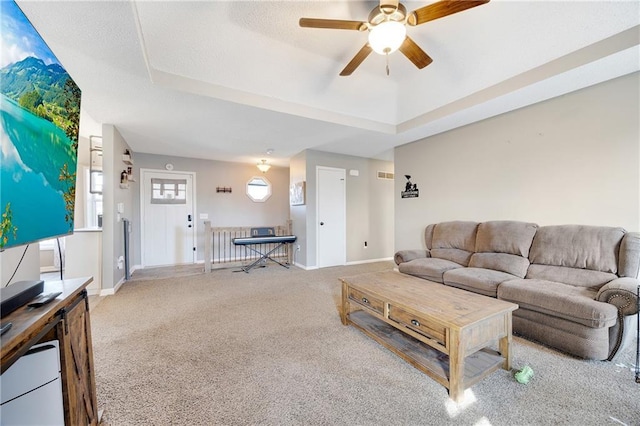 carpeted living room with ceiling fan, baseboards, and a raised ceiling