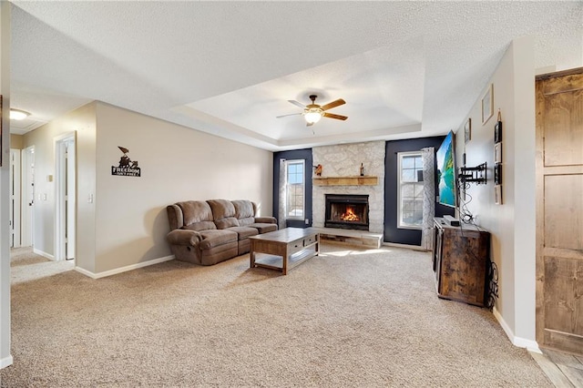 carpeted living room featuring baseboards, ceiling fan, a tray ceiling, a textured ceiling, and a fireplace