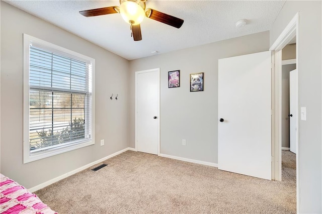 unfurnished bedroom with carpet, visible vents, a textured ceiling, and baseboards