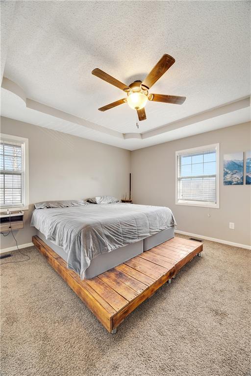 carpeted bedroom featuring a ceiling fan, a raised ceiling, a textured ceiling, and baseboards