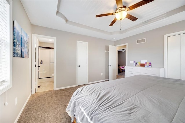 bedroom featuring baseboards, visible vents, a raised ceiling, light colored carpet, and two closets