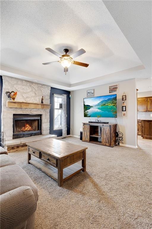 living area featuring a textured ceiling, a fireplace, baseboards, carpet, and a raised ceiling