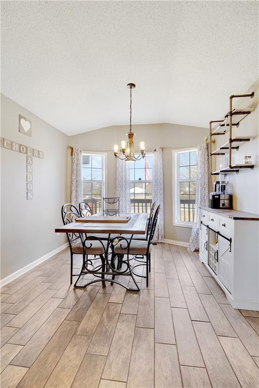 dining space with a notable chandelier, lofted ceiling, light wood-style flooring, a textured ceiling, and baseboards