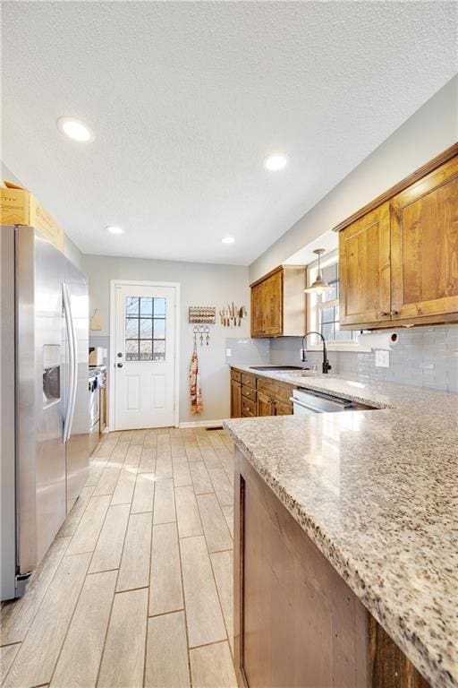 kitchen featuring tasteful backsplash, brown cabinetry, stainless steel fridge with ice dispenser, wood finish floors, and a sink