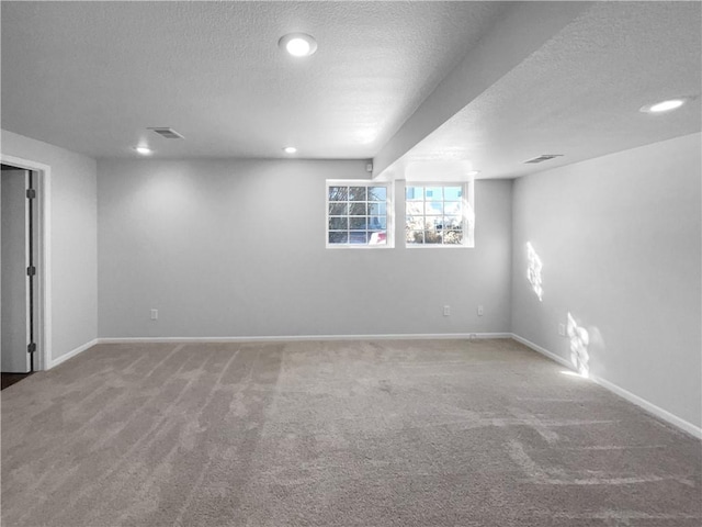 basement with a textured ceiling, carpet flooring, visible vents, and baseboards