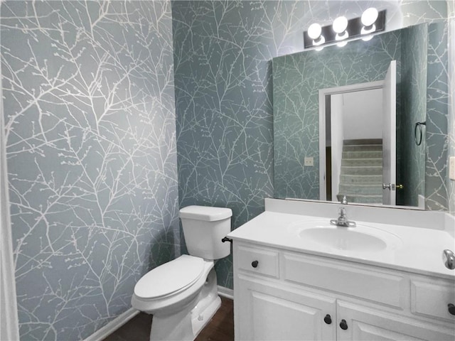 half bathroom featuring toilet, vanity, and wallpapered walls