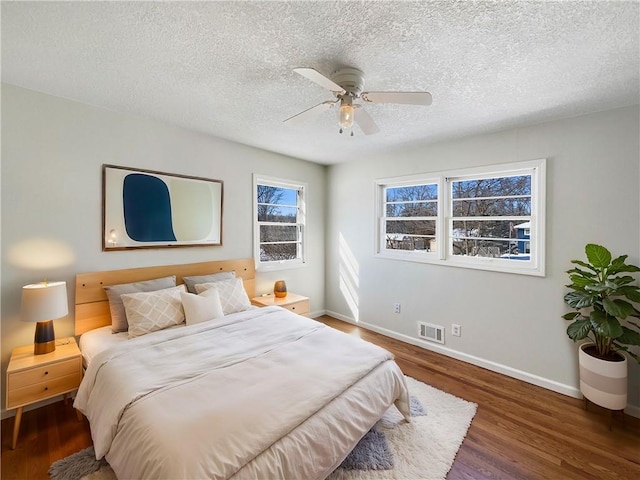 bedroom featuring a textured ceiling, wood finished floors, a ceiling fan, visible vents, and baseboards