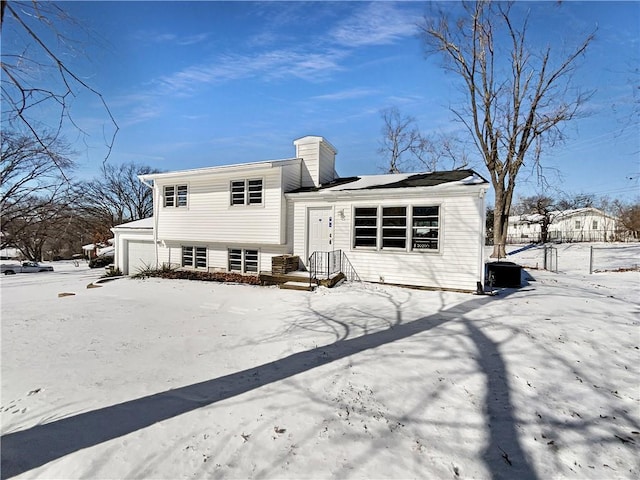 snow covered property featuring a garage, a chimney, and fence