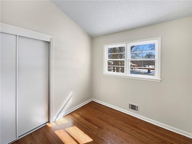 unfurnished bedroom featuring a textured ceiling, a closet, wood finished floors, and visible vents