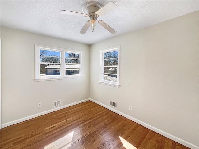 empty room featuring a textured ceiling, visible vents, and wood finished floors